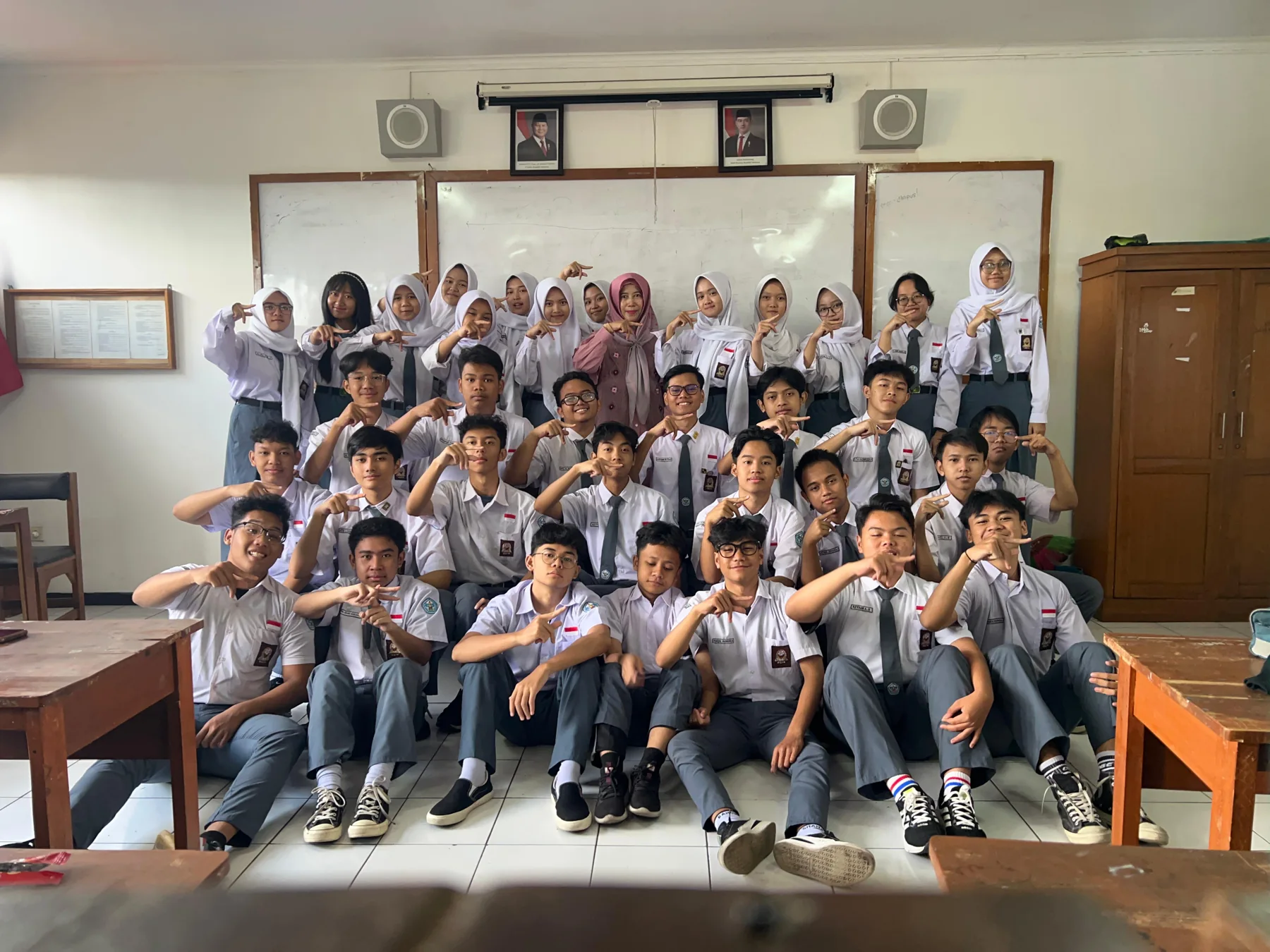 Teman-teman kelas berpose bersama di depan papan tulis.
